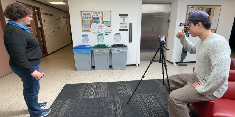 Student looking at a phone on a tripod giving a thumbs up to another person.