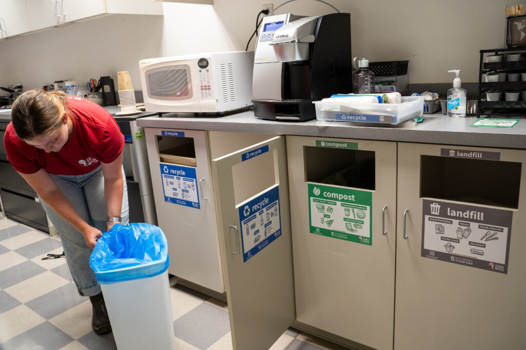 Person putting a blue bag into a recycling bin