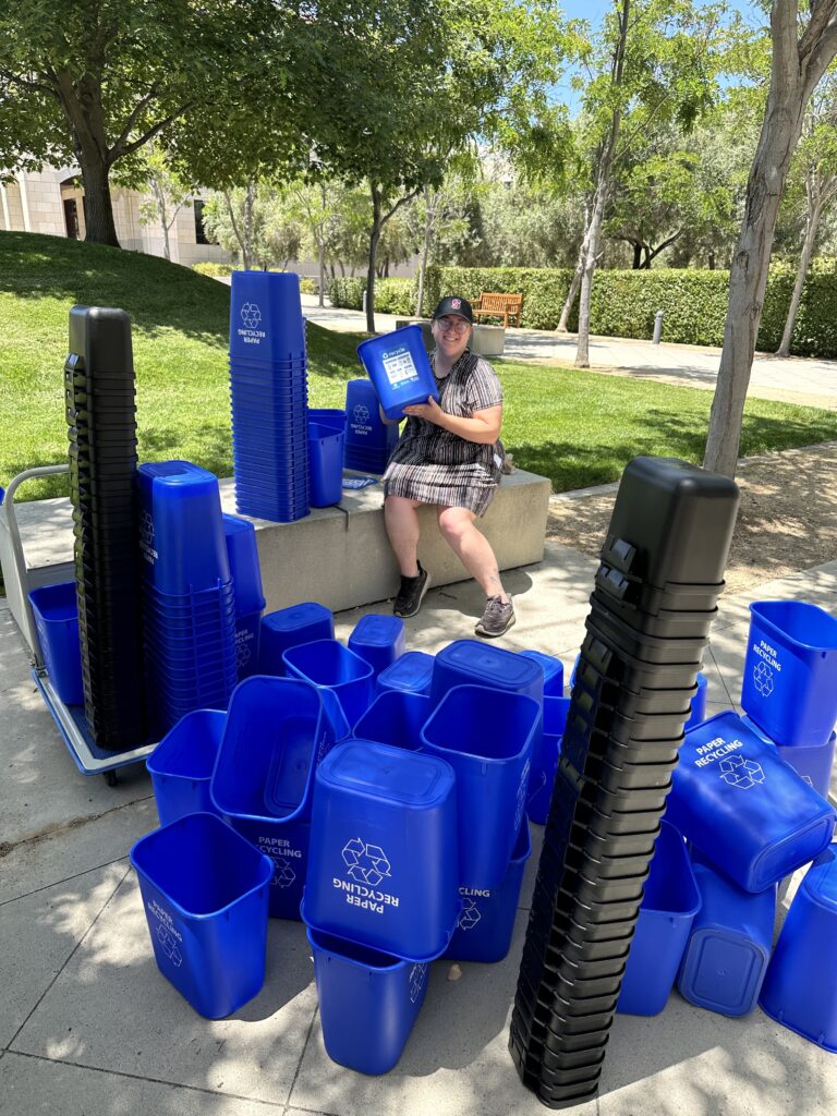 Person sitting outside with stacks of blue and black bins.