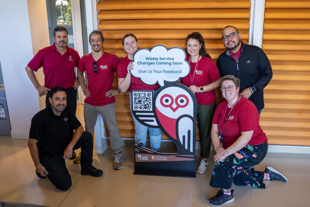 Seven people standing with cut-out of owl that says "Waste Service Changes Coming Soon"