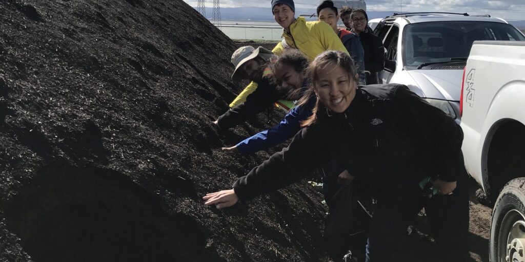 Students reaching hands into a large pile of compost