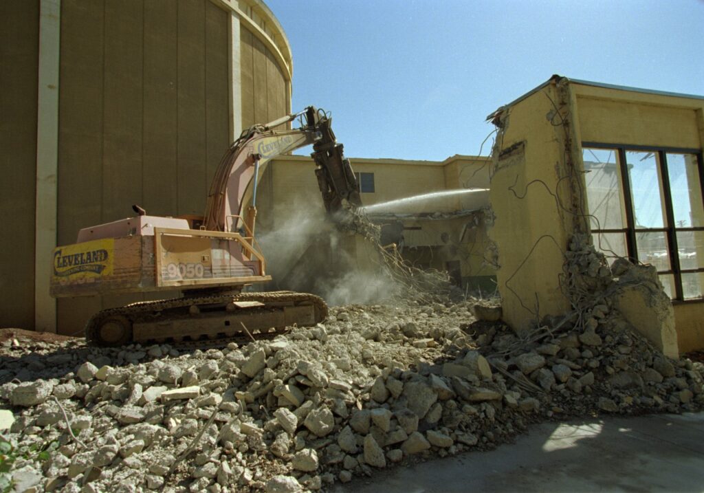Construction vehicle sitting on pile of rubble knocking down remaining portions of the physics tank