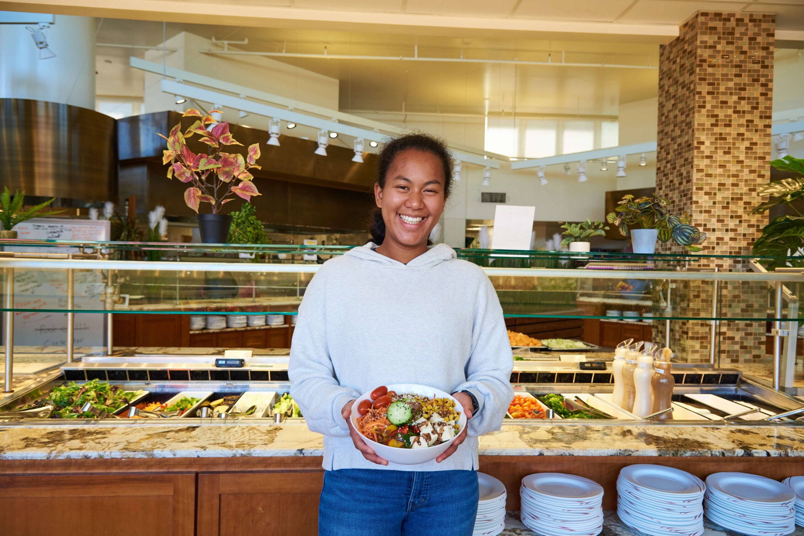 Female student smiling, standing and holding salad from campus salad bar