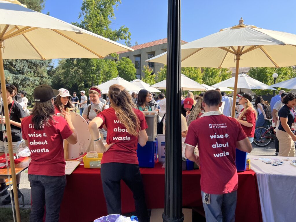 Back of three people behind a table talking to students about how to dispose of waste outside