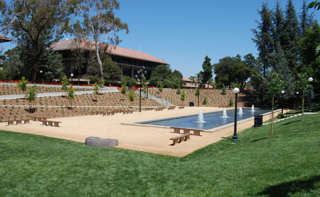 Park with sloping lawn leading to water feature with benches