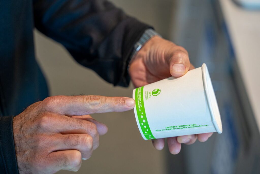 Person pointing at cup labeled compostable