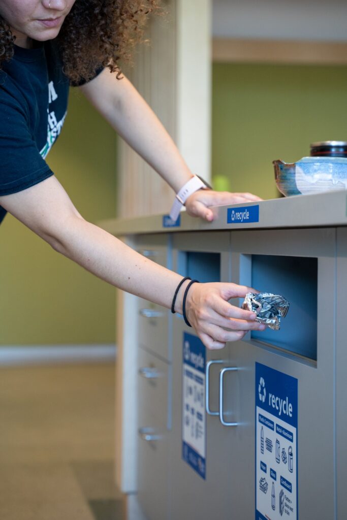 A person putting a ball of aluminum foil into the recycling bin