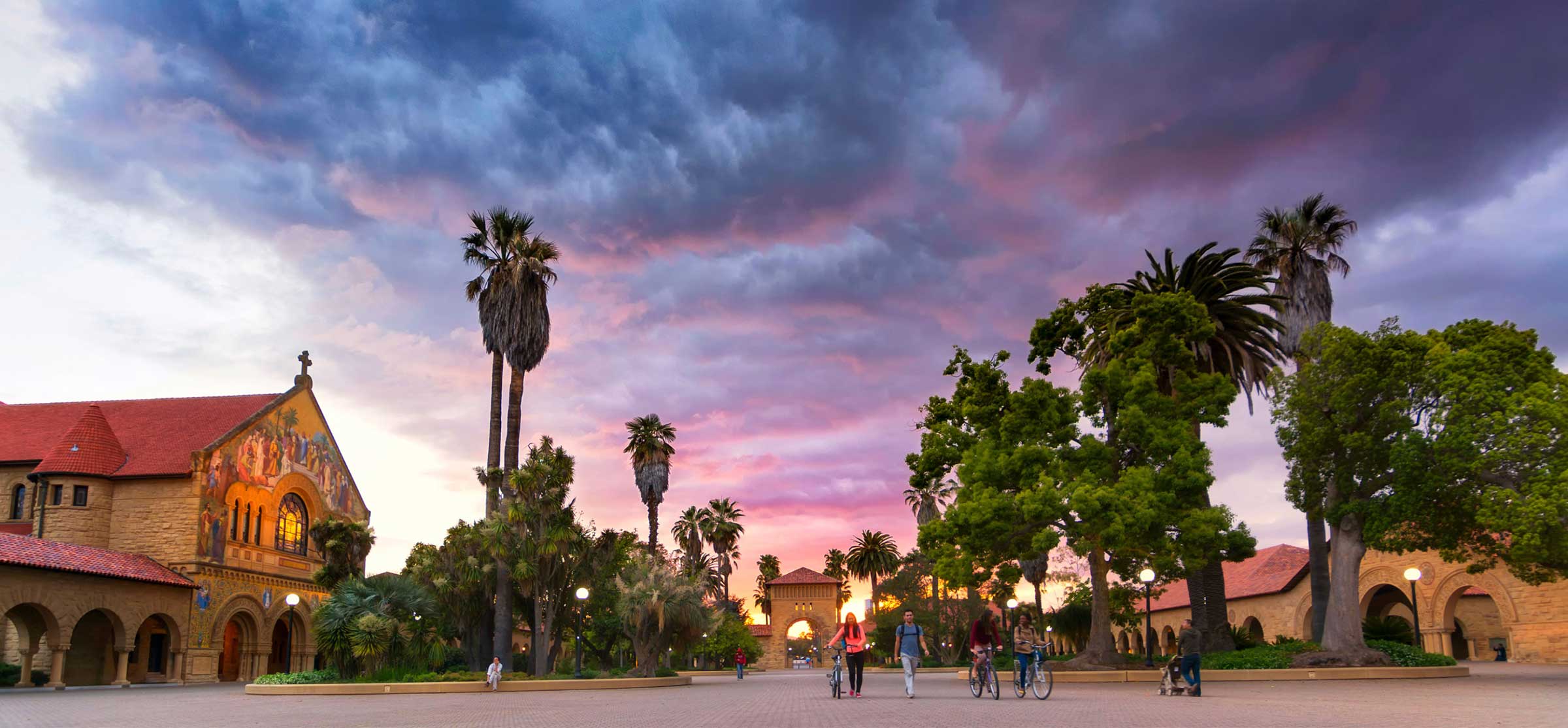 Students walk and bike around Stanford's campus, under a beautiful sunset.