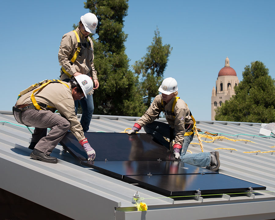 Workers install solar panels on a Stanford Campus rooftop.