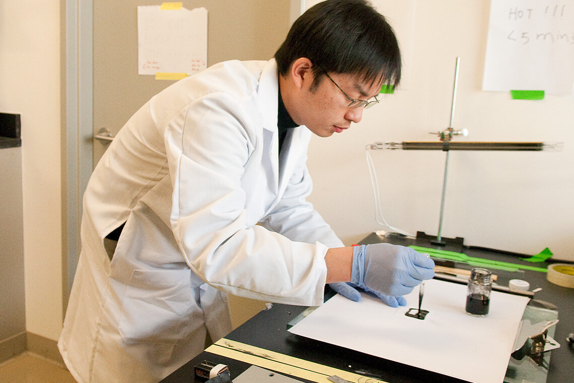 Bing Hu, a post-doctoral fellow, prepares a small square of ordinary paper to with an ink that will deposit nanotubes on the surface that can then be charged with energy to create a battery.
