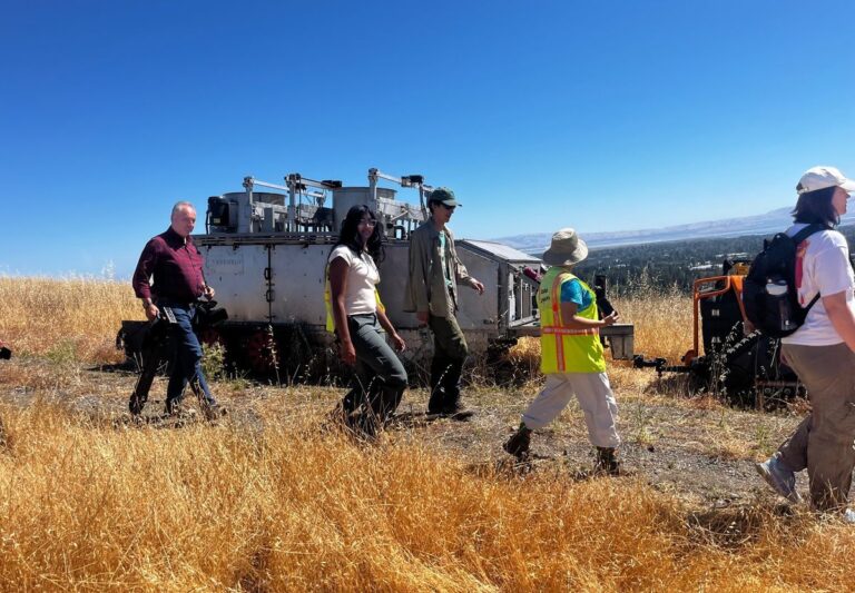 Six people including conservation program staff, student observers, and a member of the press walking through Stanford’s open land next to the "BurnBot" machine