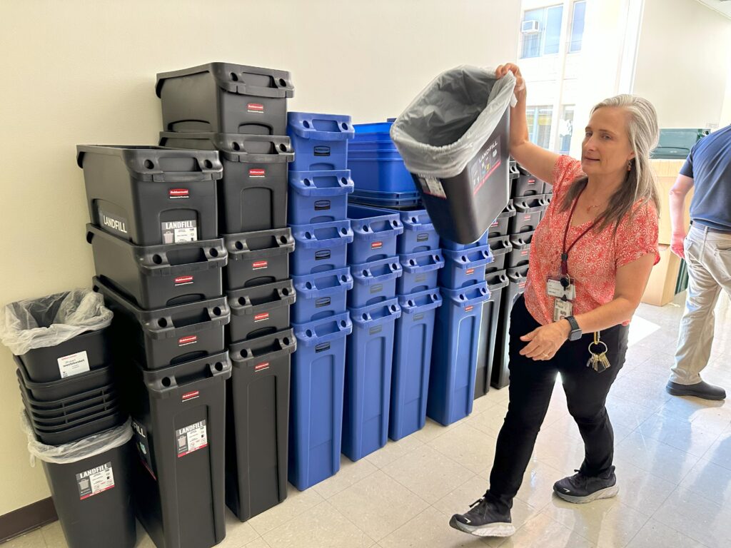 Person moving a landfill bin with dozens of black and blue bins in the background.