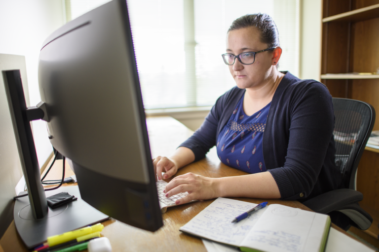 Person sitting behind a computer monitor typing on a keyboard
