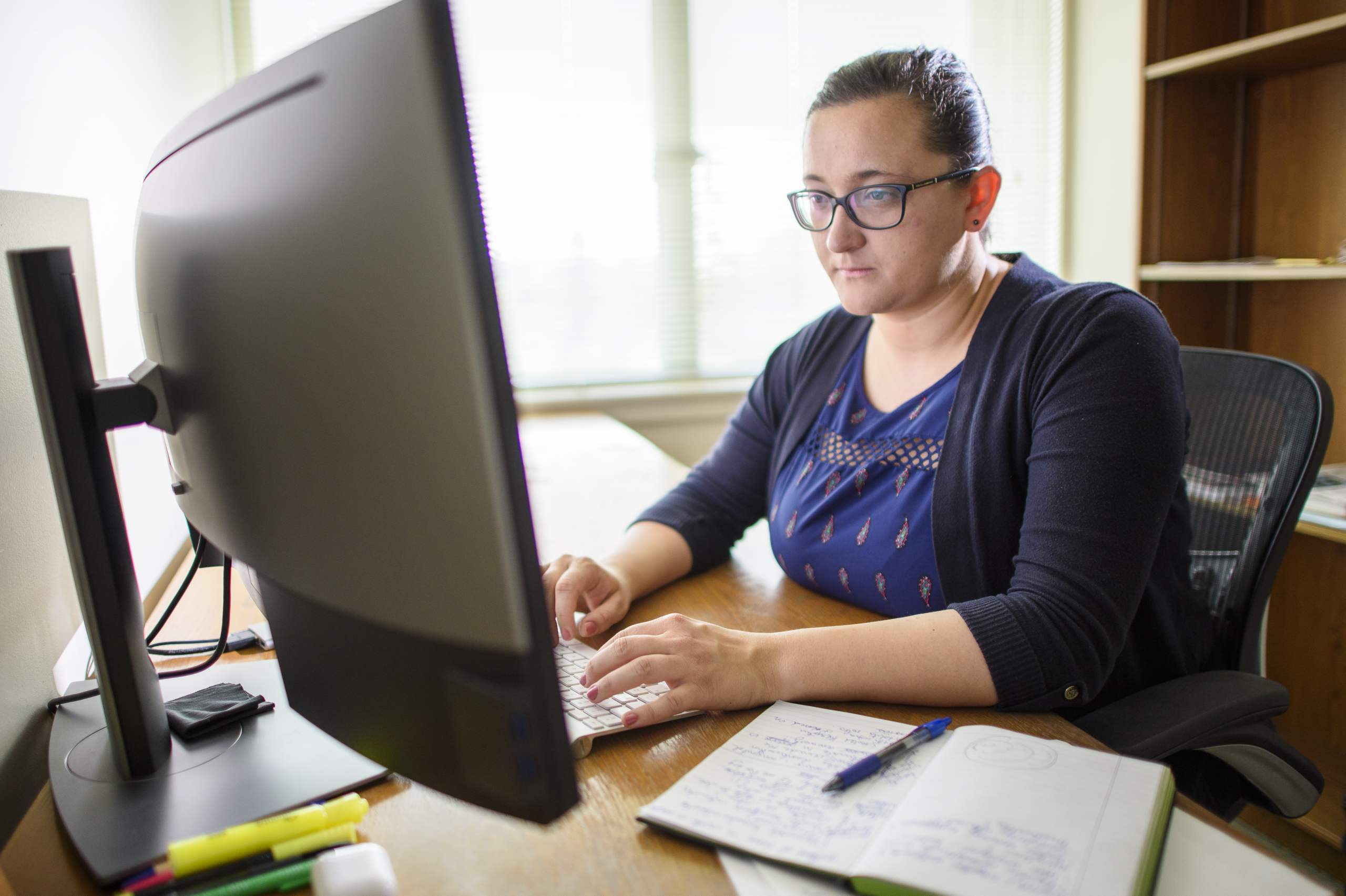 Person sitting behind a computer monitor typing on a keyboard