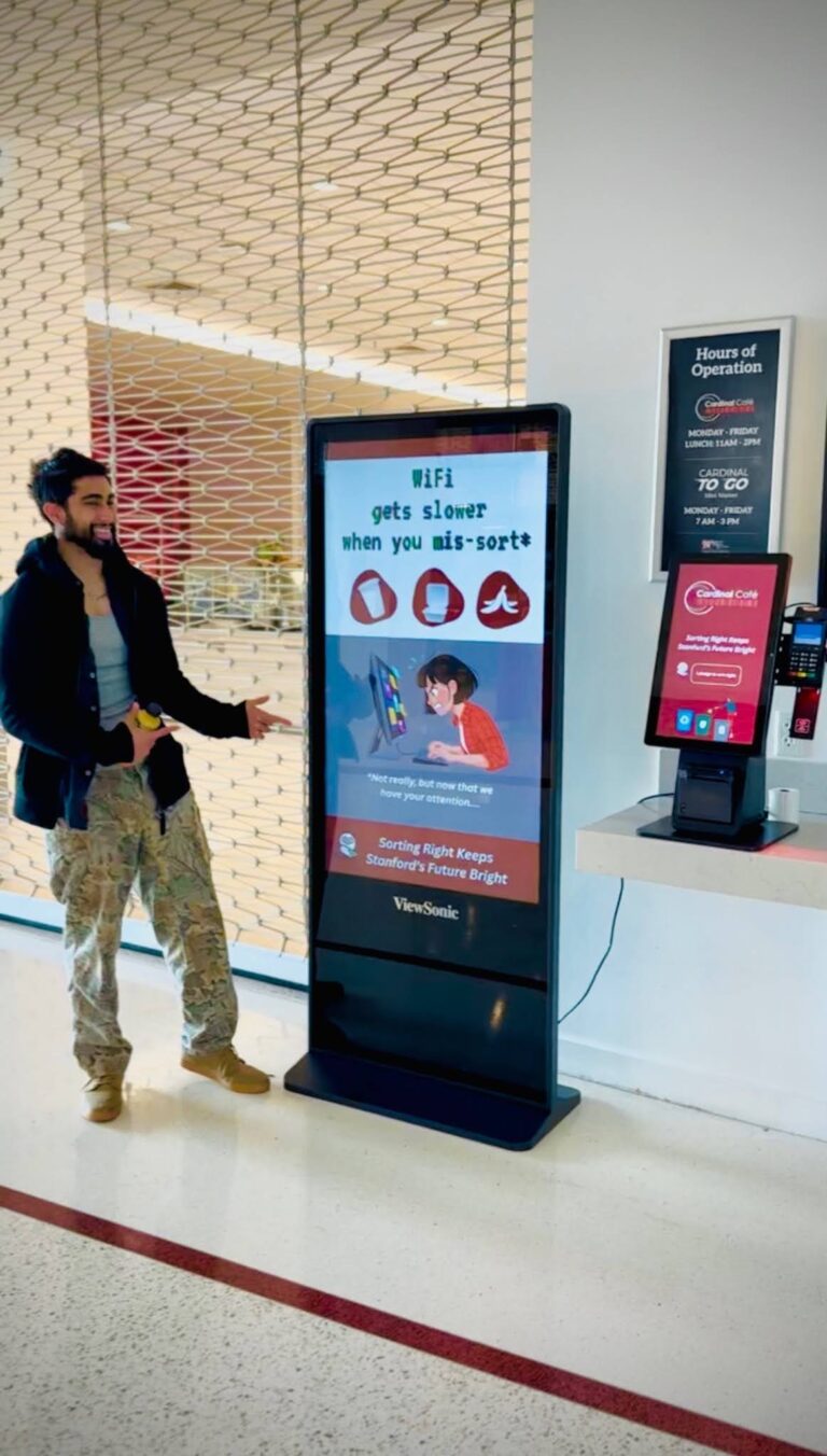 A student standing next to a pointing to a digital sign that says "Wifi gets slower when you mis-sort"